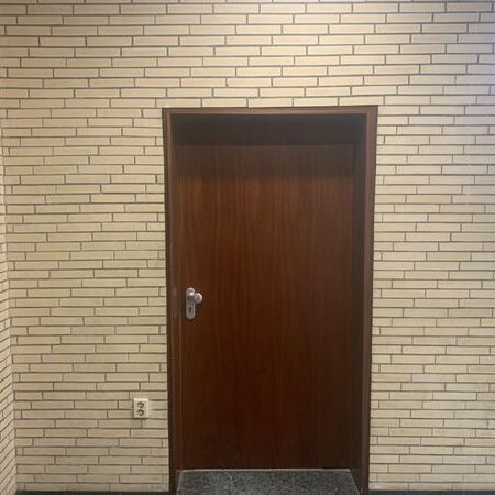 Brandschutztür mit silbernem Griff und rotem Feuerlöscher-Schild daneben. Treppe rechts im Bild