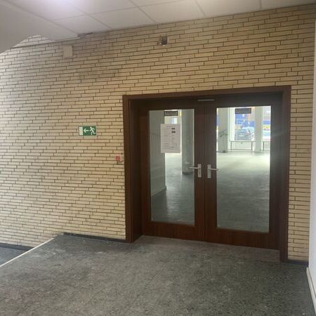 "Brandschutztür mit Glasfenster und Notausgangsschild darüber. Fliesenboden und Leuchte an der Wand