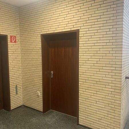 "Brandschutztür mit Glasfenster und Notausgangsschild darüber. Fliesenboden und Leuchte an der Wand