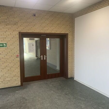 "Brandschutztür mit Glasfenster und Notausgangsschild darüber. Fliesenboden und Leuchte an der Wand