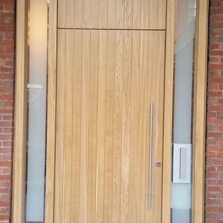 Ansicht einer modernen Holz-Eingangstür mit einem vertikal ausgerichteten, schmalen Fenster und Edelstahlbeschlägen, eingebaut in eine Backsteinwand