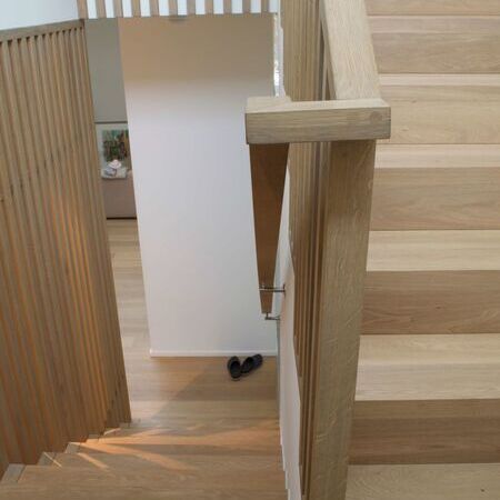 Holztreppe mit einem Holzgeländer, vertikale Holzlattenwand im Hintergrund, und Hausschuhe auf dem Boden