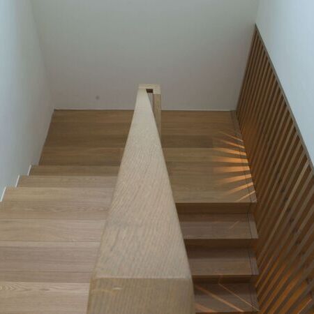 Ansicht der Treppe von oben, mit Holzstufen und einem vertikal angeordneten Holzgeländer an der Wandseite