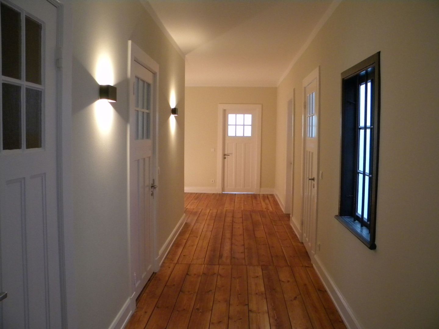 Ein Flur in einem sanierten Altbau mit Holzboden, weiß gestrichenen Türen und Wandleuchten, die weiches Licht werfen