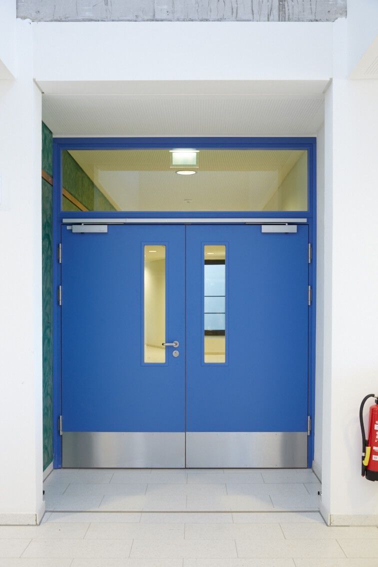 Ansicht einer blauen Brandschutztür mit Oberlicht und Notausgangszeichen