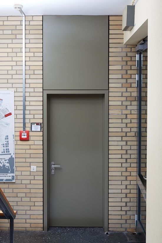 Brandschutztür in einem historischen Gebäude, grau lackiert, mit umliegendem Backsteinmauerwerk und Sicherheitsbeschilderung