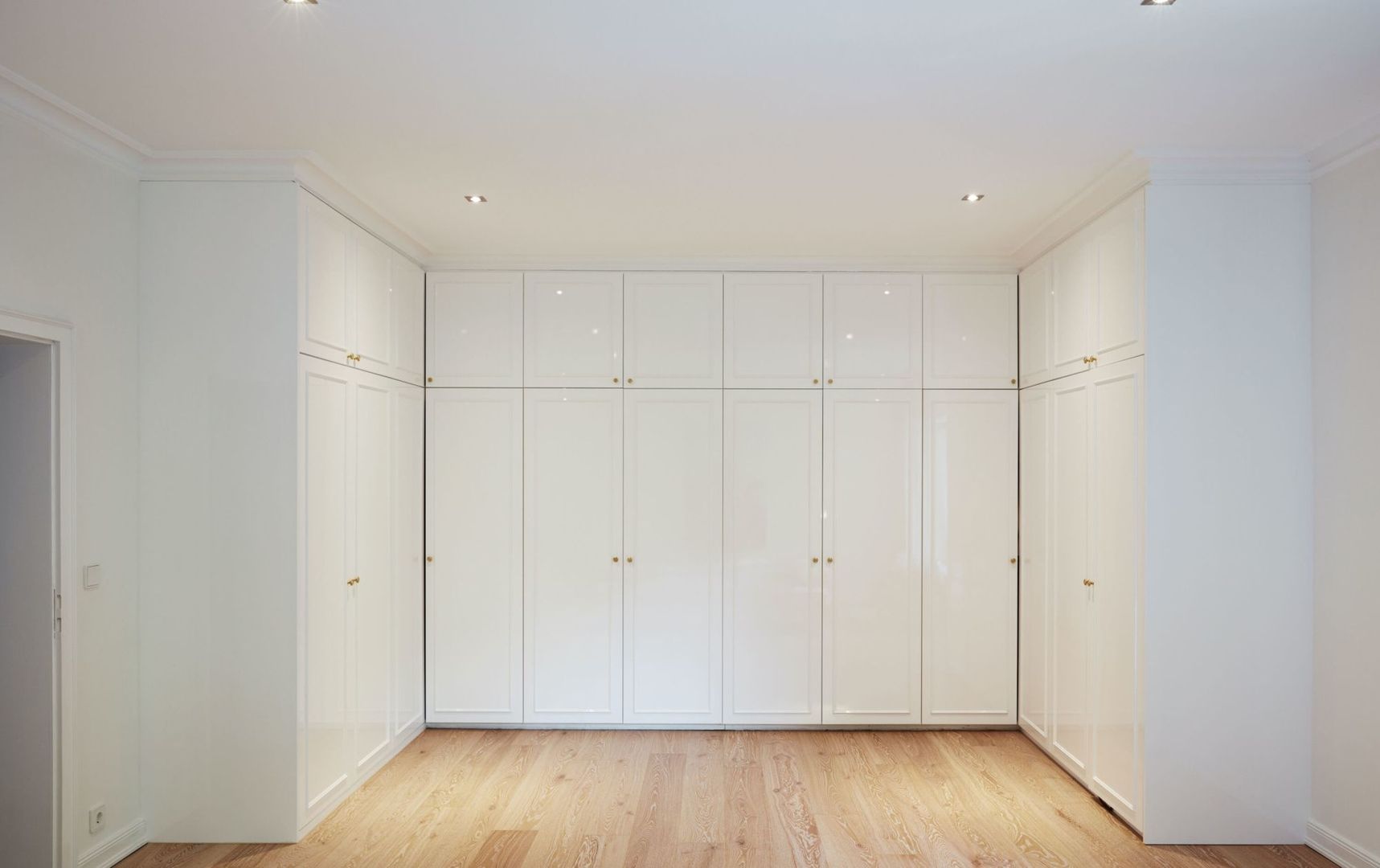 Hochwertiger dreiseitiger Einbauschrank mit lackierten weißen Fronten, ausgestattet mit goldenen Messingknöpfen. Der Schrank bietet sowohl Einlegeböden als auch Kleiderstangen für viel Stauraum