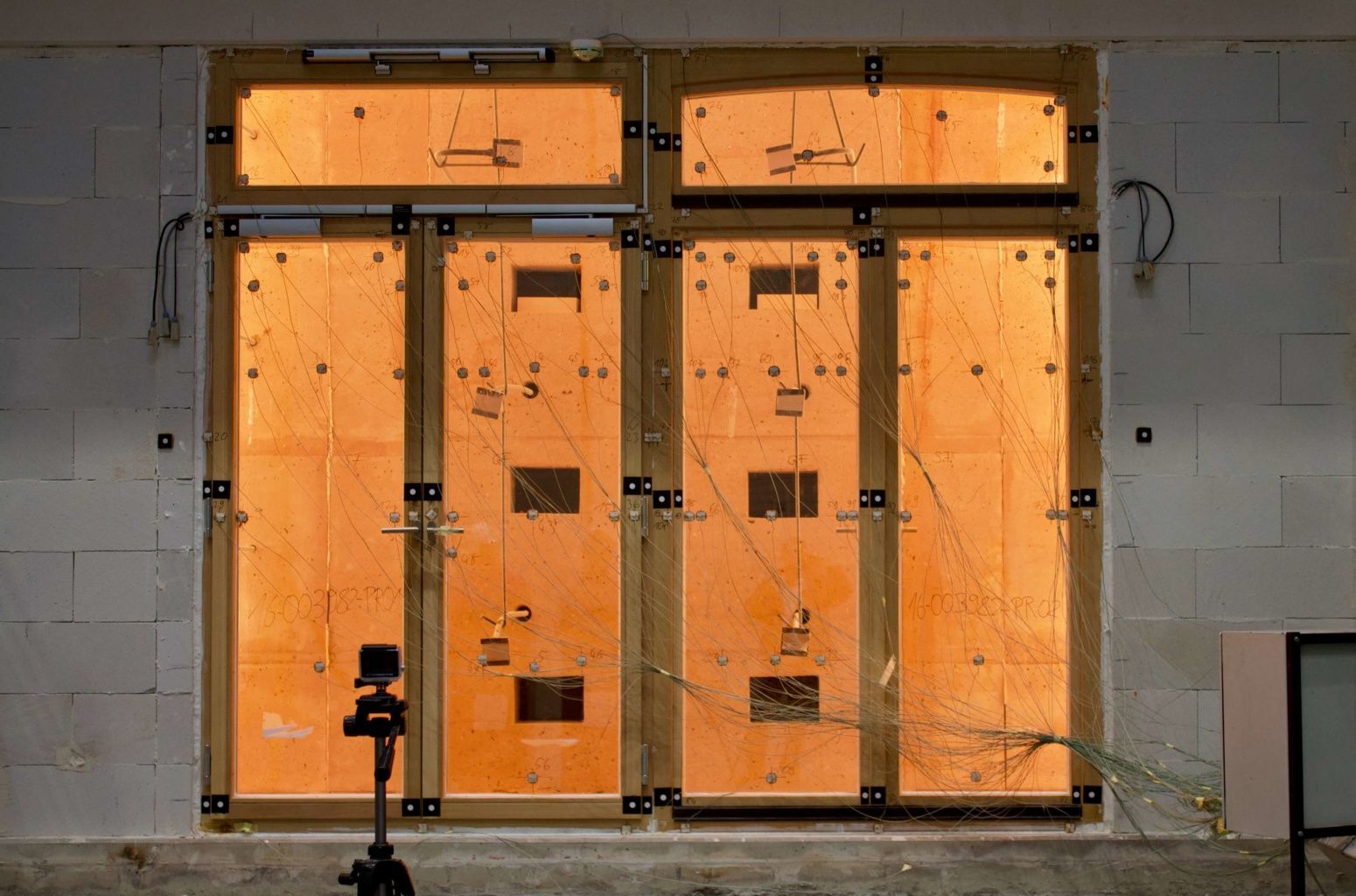 Brandschutzfenster in einer Testumgebung mit Verkabelung und Sensoren, dahinter orangefarbene Beleuchtung