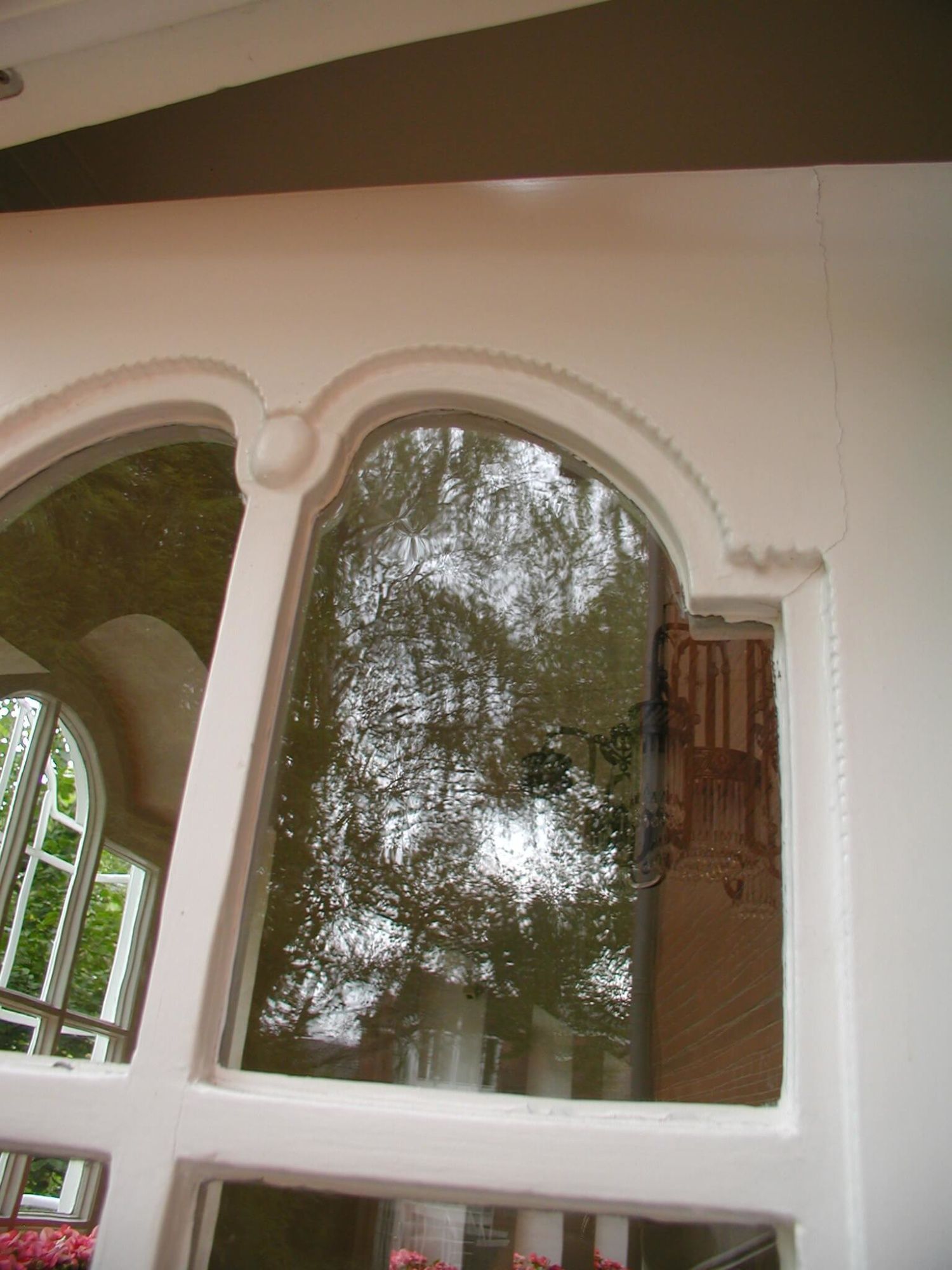 Detailaufnahme eines Fensters mit einem runden oberen Bogen und verzierter Fensterumrandung, die die Bäume draußen reflektieren