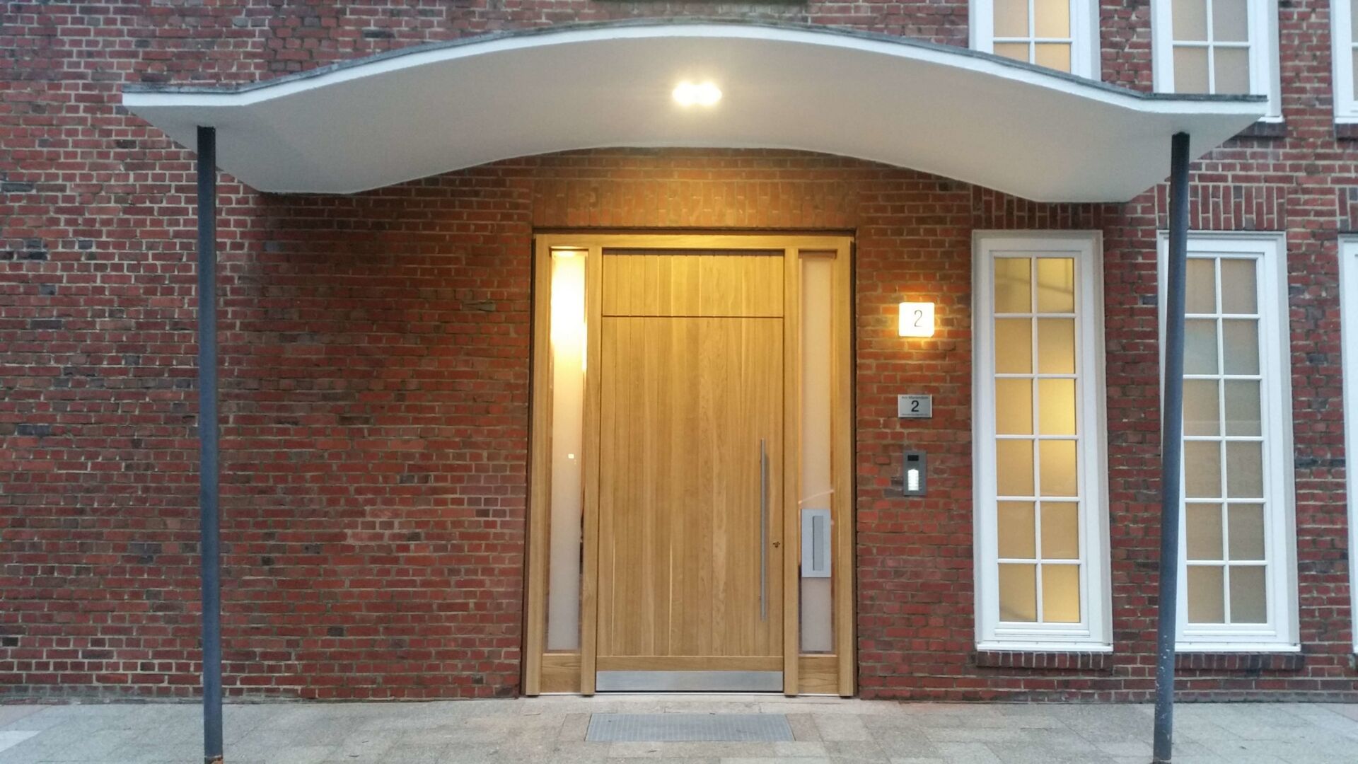 Gesamtansicht einer modernen Holz-Eingangstür mit einem schlanken Edelstahlgriff und seitlichen Glaseinsätzen