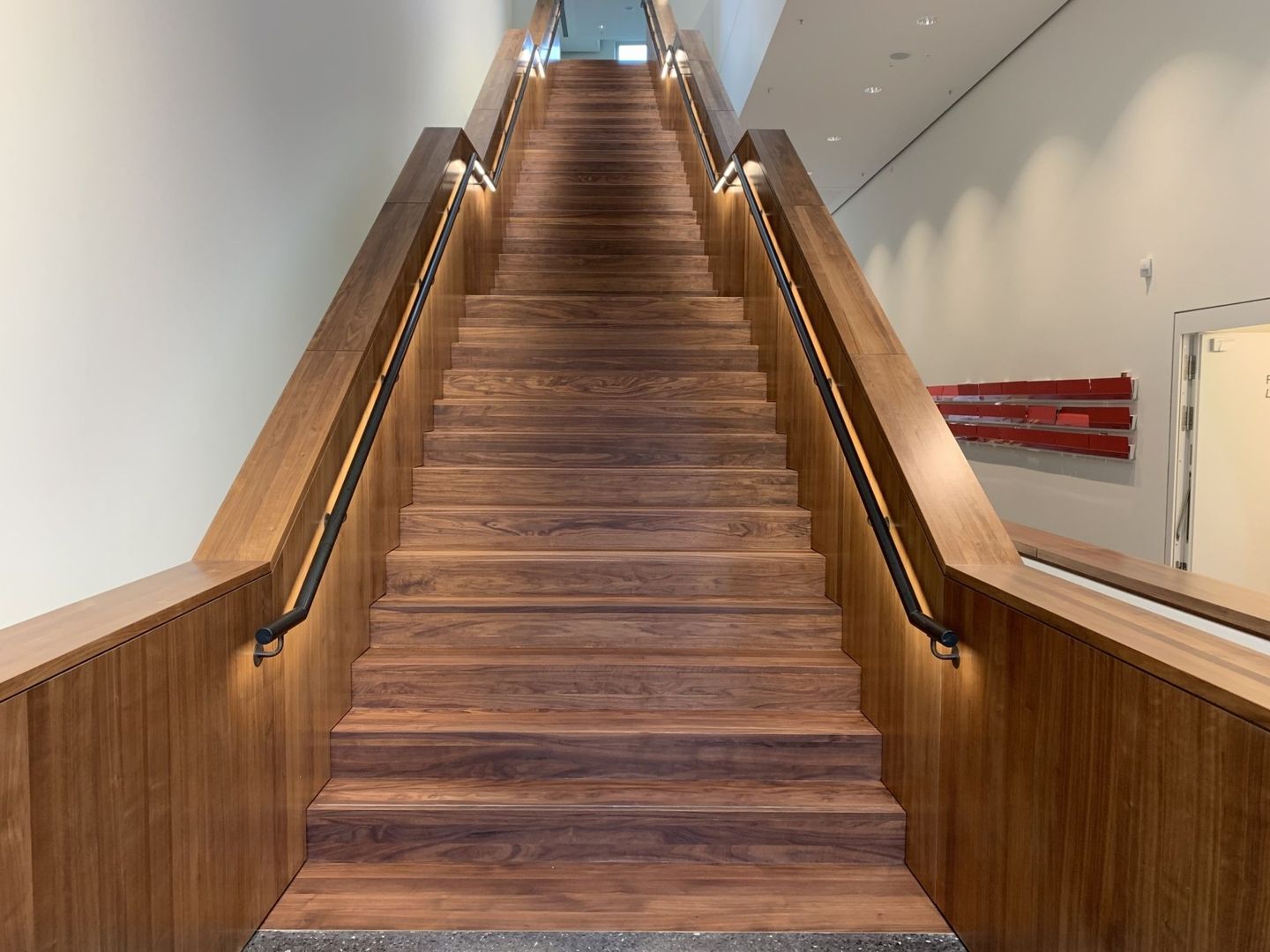 Holztreppe mit moderner LED-Beleuchtung und eleganten Handläufen aus Metall, ideal für öffentliche Gebäude oder Unternehmen, mit durchgeführter Oberflächenbehandlung