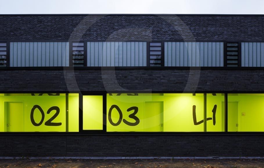 Außenansicht eines modernen Gebäudes mit großen Fenstern, die von grünen Wänden hinterlegt sind, auf denen große Zahlen (02, 03, L1) zu sehen sind