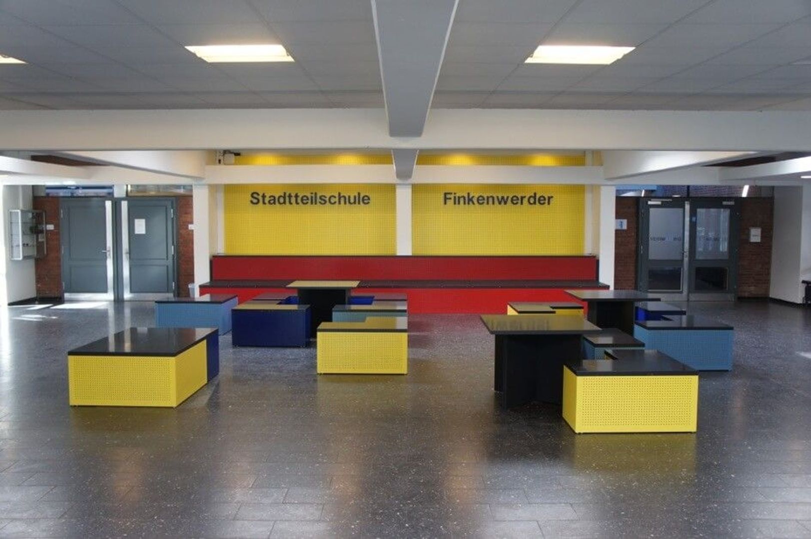Innenansicht der Stadtteilschule Finkenwerder mit bunten Sitzgelegenheiten in Gelb, Blau und Schwarz vor einer gelben Wand