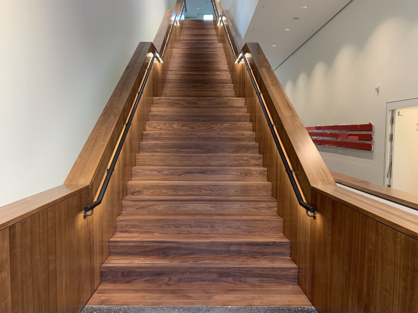 Holztreppe mit seitlichen Handläufen und integrierter Beleuchtung, führt in einem modernen Gebäude nach oben