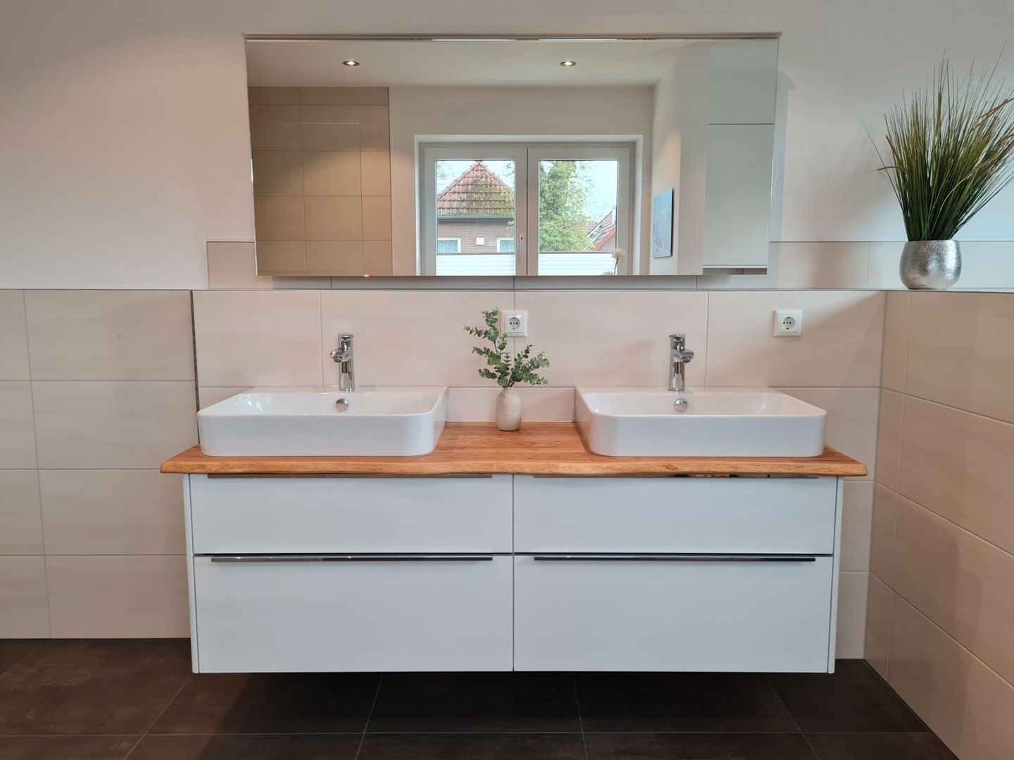 Modernes Badezimmer mit zwei weißen Aufsatzwaschbecken auf einer Holzplatte, dekoriert mit Pflanzen und großem Spiegel im Hintergrund